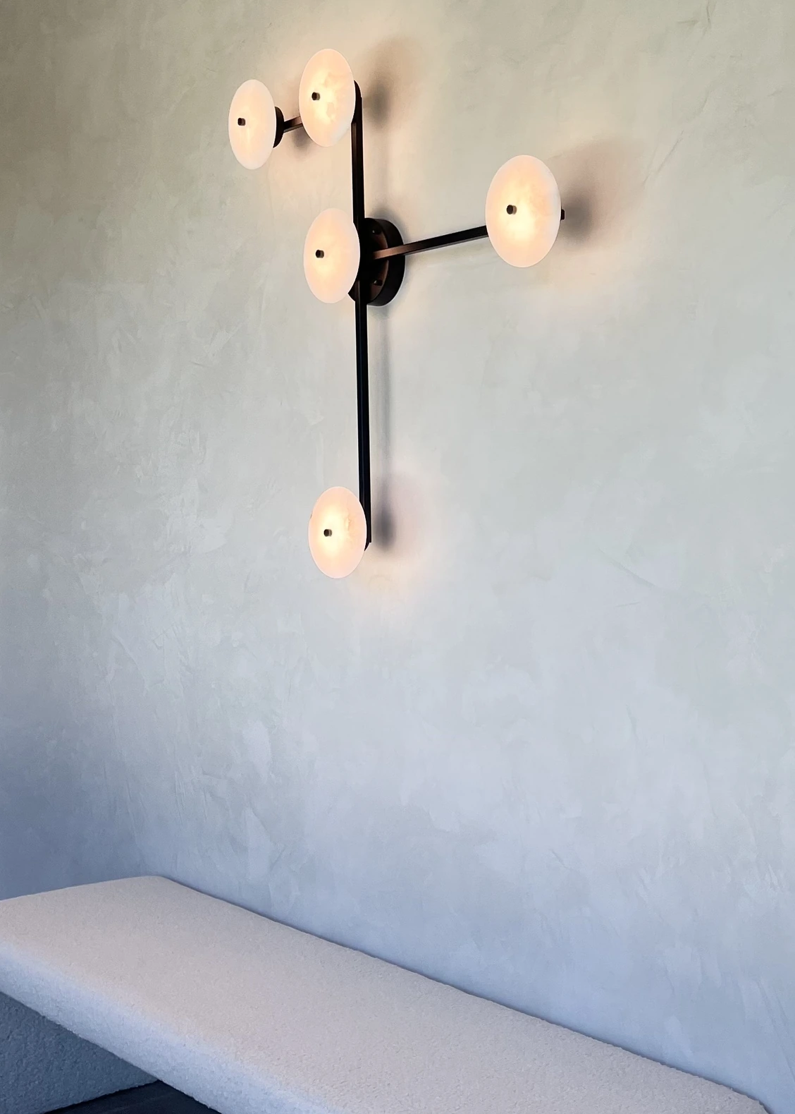 Smooth natural lime plaster wall with a sculptural wall sconce above a curved white bench