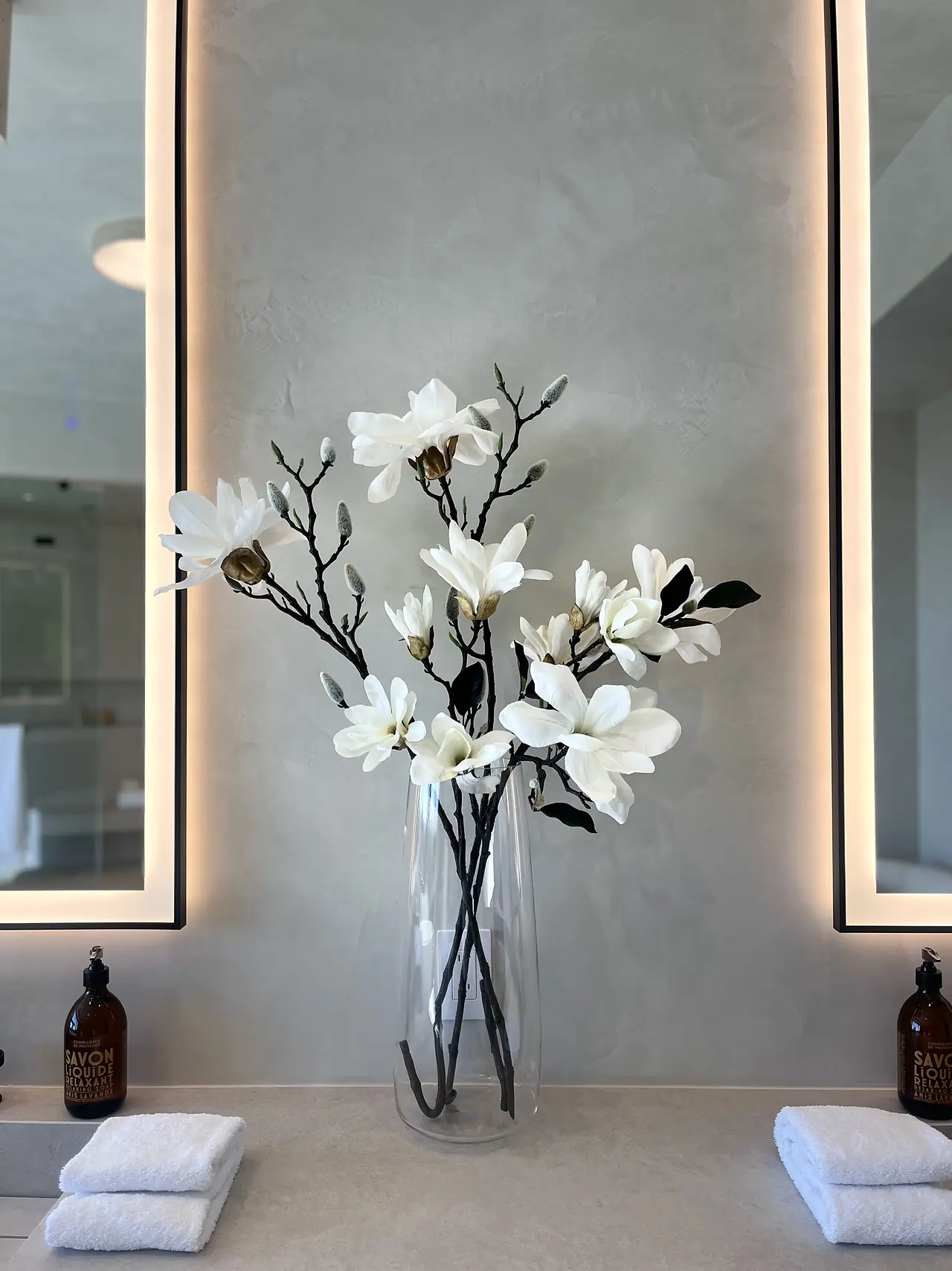Bathroom vanity wall in soft plaster between two backlit mirrors